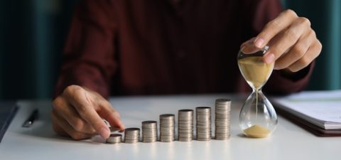 Rising,Stack,Of,Coins,And,Running,Sand,Clock,On,The